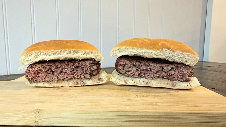 A close-up of a burger cut in half on a wooden cutting board, showing a brown interior that has a slightly pink hue