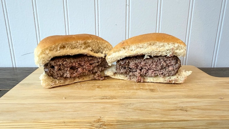 A close-up of a burger cut in half on a wooden cutting board, showing a slightly pink center