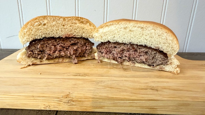 A close-up of a burger cut in half on a wooden cutting board, showing a very slightly pink center