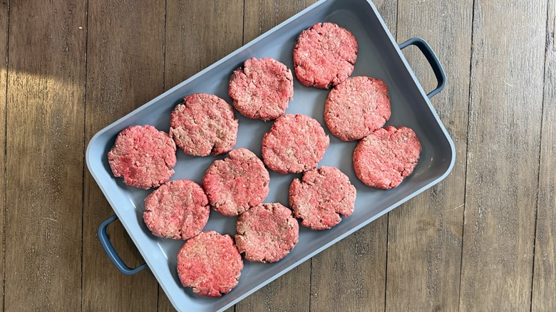 An overhead shot of a blue oven pan with 12 raw burger patties on a wood table