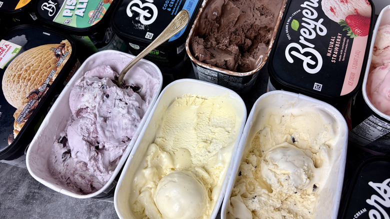 Tubs of Breyers ice cream are lined up on the counter, a spoon sticking out of one of them