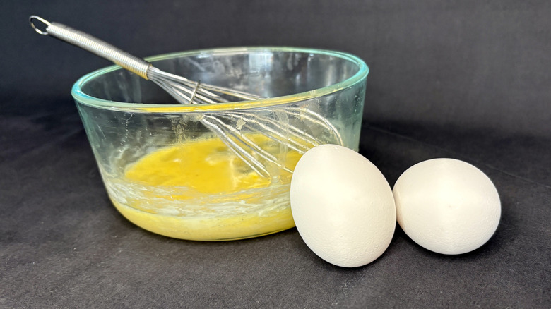 Bowl of whisked eggs next to two whole eggs