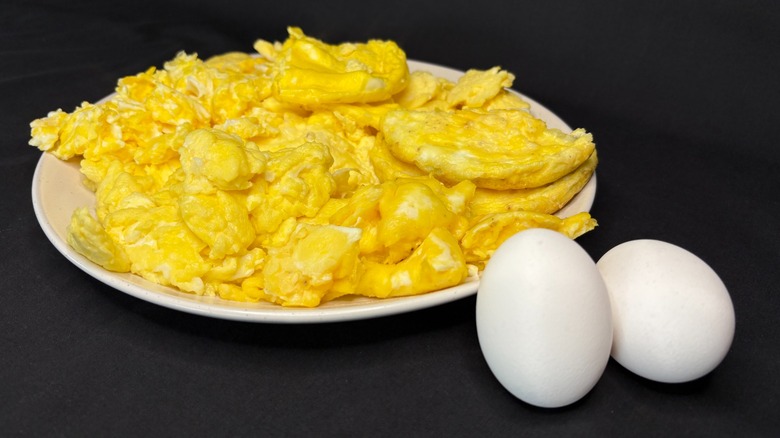 Scrambled eggs on plate, two whole eggs in front