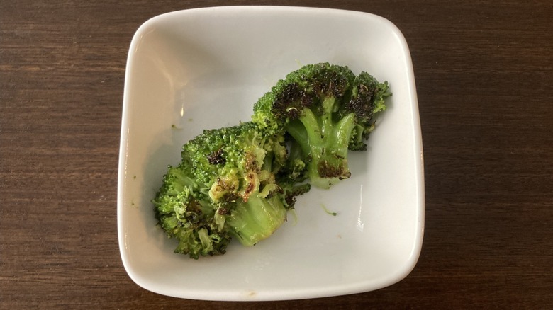 Two florets of stir fried broccoli in a white bowl