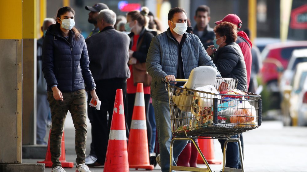 Shopper leaving grocery store with line of customers outside