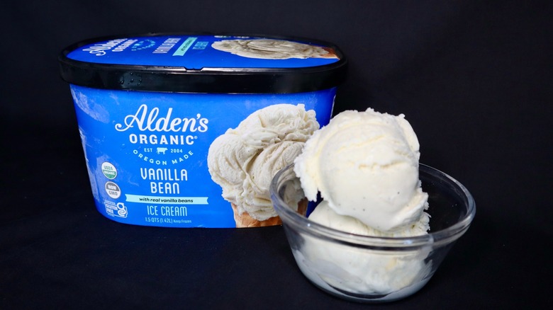 A carton of vanilla ice cream next to a small bowl with two scoops.
