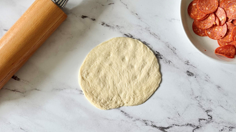 Rolled out dough ball next to rolling pin and pepperoni slices
