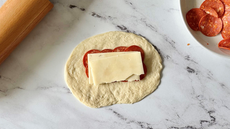 Rolled out dough with pepperoni and cheese slices on top