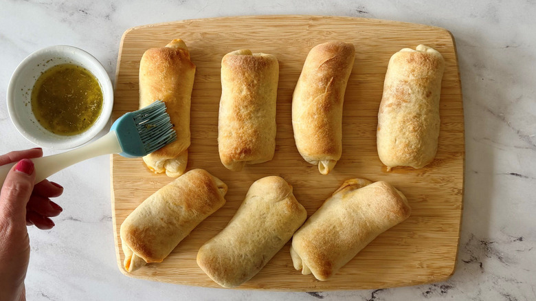Brushing baked pepperoni rolls with seasoned butter