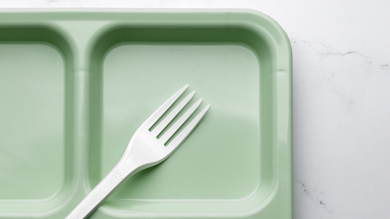 A plastic fork on a green plastic school lunch tray on a white surface.