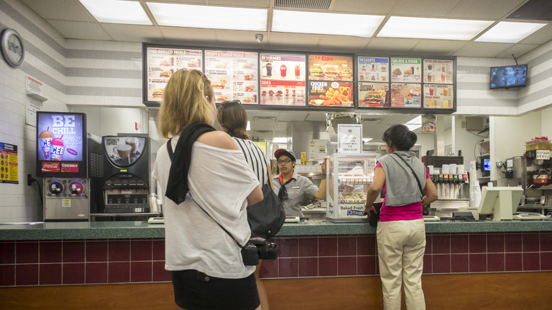 People wait in line at the register in front of a menu board inside a Burger King
