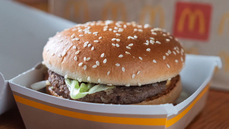 A Big Mac sits in an open McDonald's container, with a McDonald's bag in the background.