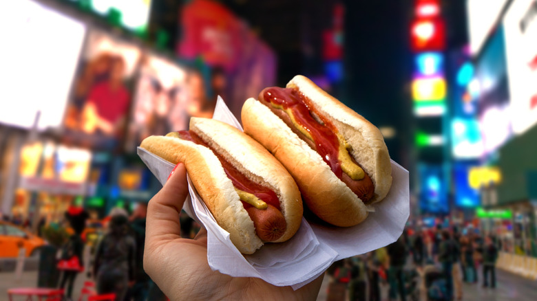 Hand holding hot dogs in Times Square at night
