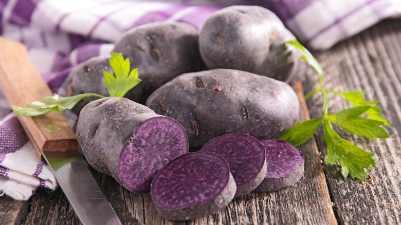 purple potatoes and rag with parsley sprigs and knife on wood board