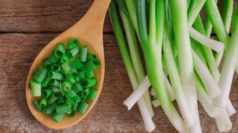 Spoon full of chopped scallions next to full-length scallions