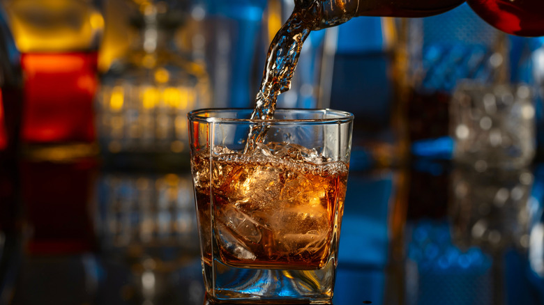 Whisk(e)y pouring into glass with ice.