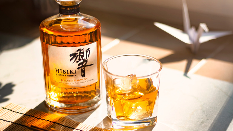 Bottle and glass of Hibiki whisky with origami crane in background.