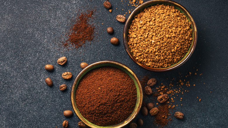 Two small bowls of ground and instant coffee with whole beans and grounds scattered beside them.