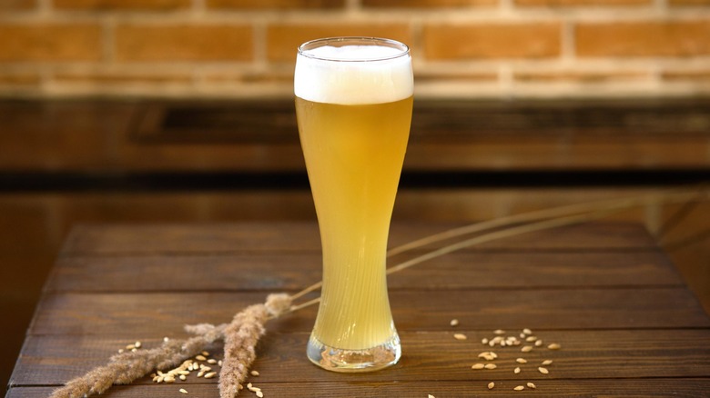 A glass of cloudy hefeweizen-style beer on a wooden table, decorated with wheat.
