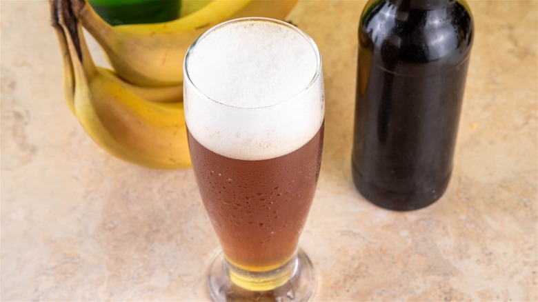 A glass of hefeweizen beer next to three bananas.