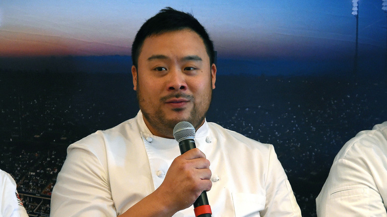 Chef David Chang wears a white chefs uniform while speaking to a microphone