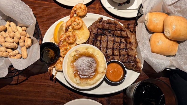 Steak, shrimp skewer, mashed potatoes with gravy, rolls, and peanuts on Texas Roadhouse table.