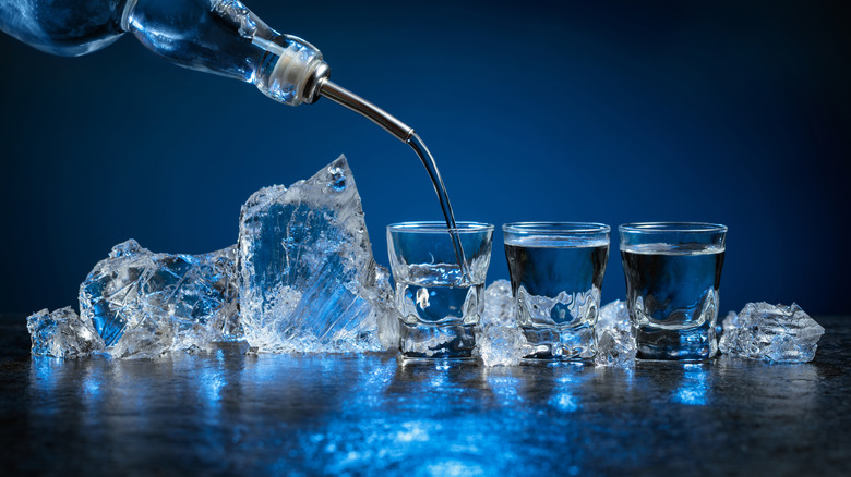 Line of three shot glasses with ice getting a pour of vodka