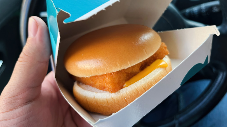 A hand holds up a slightly opened box of Filet-O-Fish inside a car