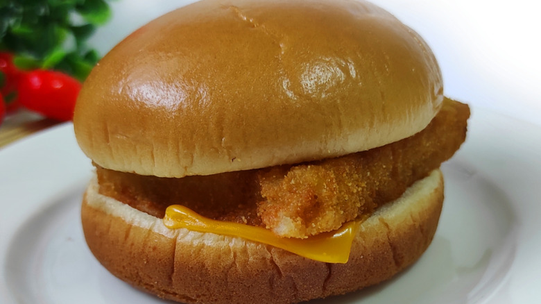 A hand shows the half-slice of cheese stuck on the top bun of a Filet-O-Fish. The rest of the sandwich is visible in the background.