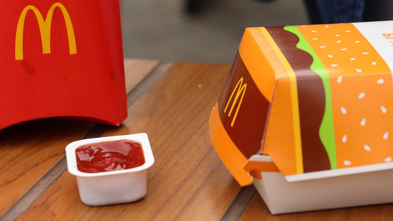 An opened ketchup cup, a McDonald's burger box, and part of a McDonald's french fries box on a table