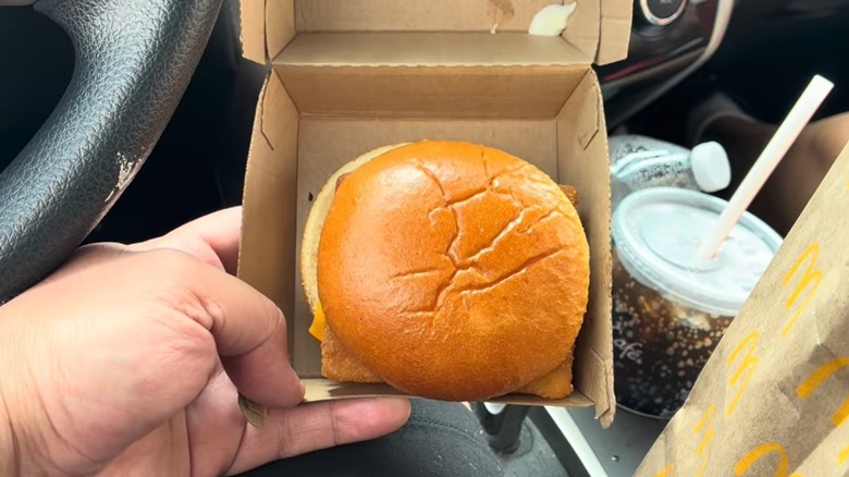 A hand holding an opened box of a Filet-O-Fish inside a car