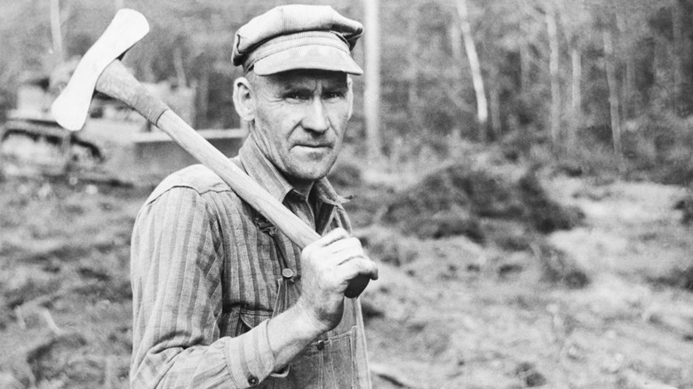 A black and white photo from 1939 of a lumberjack carrying an axe, looking straight into the camera