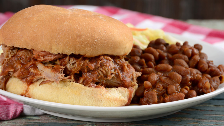 A pork sandwich with baked beans shot close-up on a plate