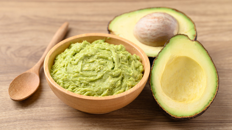 Wooden bowl of mashed avocado with cut avocado