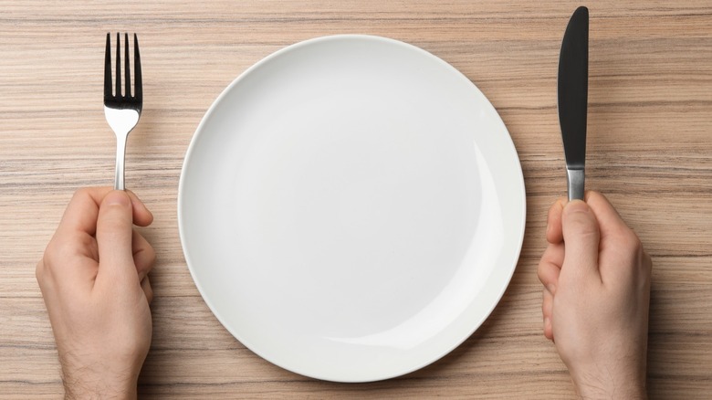 hands holding fork and knife with empty plate