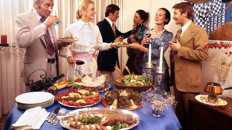 A group of people standing around a dinner table in the 1970s