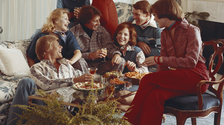 A group of people in '70s attire sitting in a vintage living room