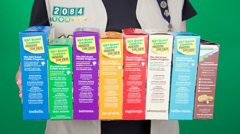 Girl Scout holding eight boxes of cookies in various flavors.