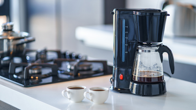 Drip coffee maker on counter with two cups of coffee