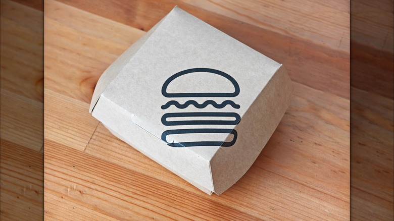 A burger box with the Shake Shack logo on a light wood table