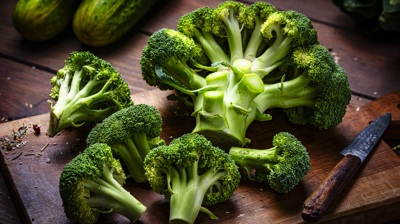 Green cut broccoli florets and a broccoli crown on a dark brown wooden cutting board.