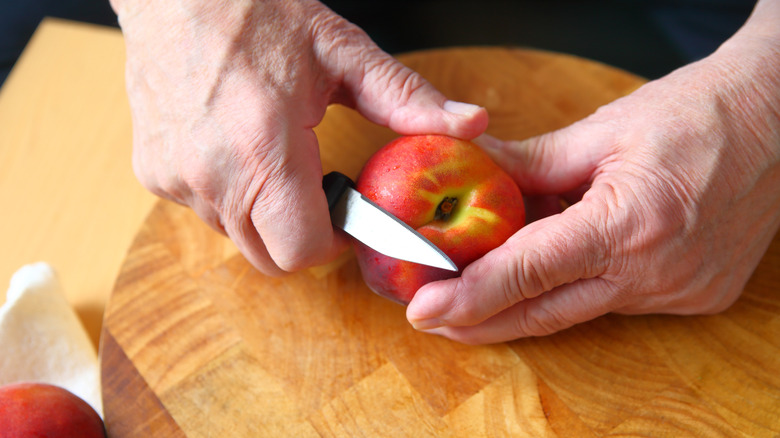 Hands using paring knife to peel fruit