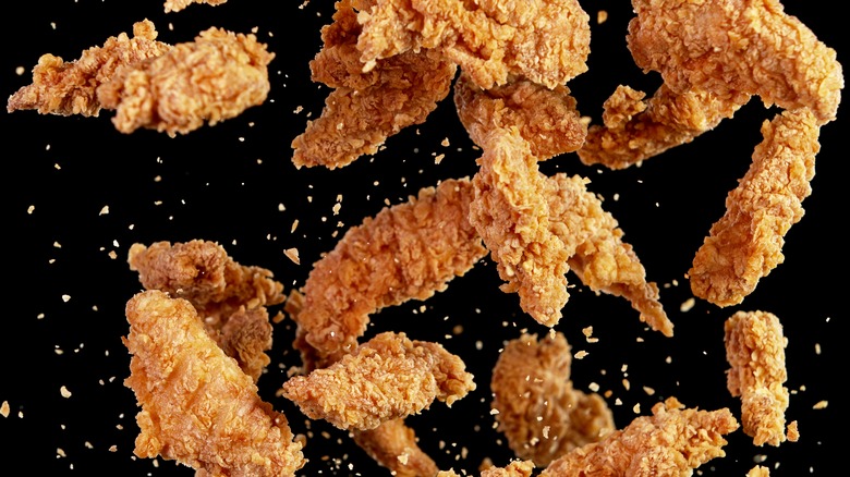 Fried chicken pieces falling over black