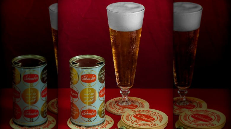 Old-school Schaefer beer can next to stacked Schaefer coasters and a glass of Schaefer beer