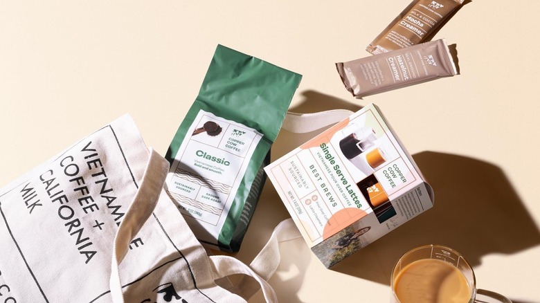 Copper Cow Coffee single serve drink box, coffee package, and seasonal creamer packages spilling out of canvas bag