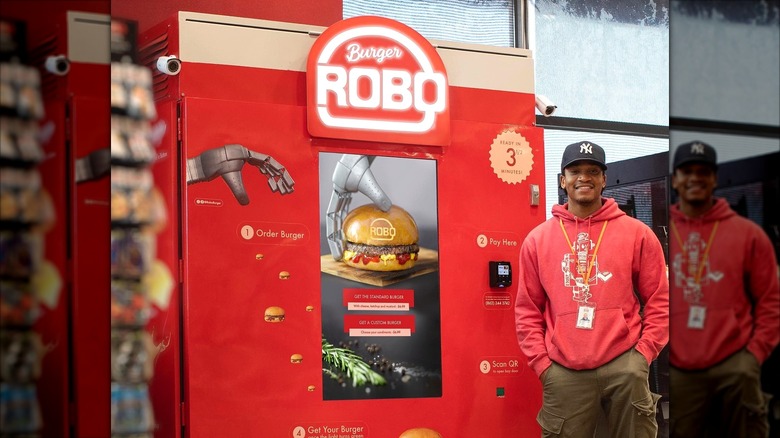a man poses with a roboburger vending machine at a truck stop