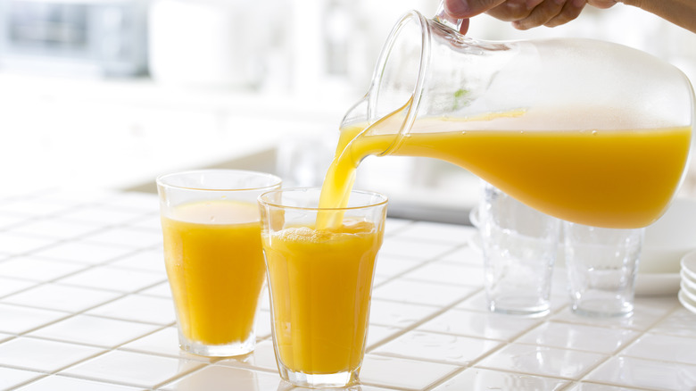 Hand pouring orange juice from pitcher