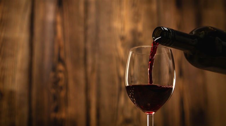 Red wine being poured into glass, wood back drop 