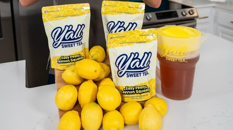 Packages of lemon Y'all Sweet Tea next to a pitcher of tea and lemons