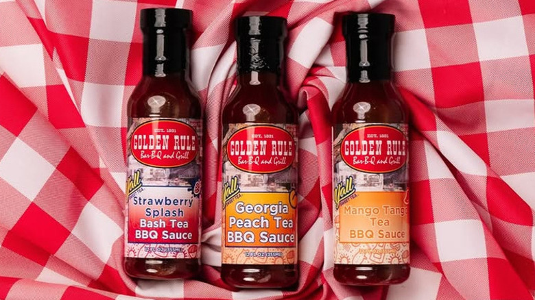 Three bottles of barbecue sauce posed on a checkered red and white picnic blanket